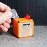 Mano insertando una púa gris en un portapúas con diseño de amplificador Orange de color naranja
