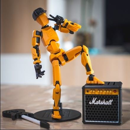 Muñeco articulado impreso en 3D en naranja, en pose de guitarrista apoyado en un amplificador en miniatura