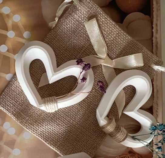 Corazones decorativos impresos en 3D en PLA blanco, atados con cordel sobre un saquito de arpillera para una boda